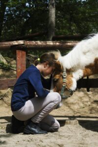 A young girl lovingly interacts with a pony outdoors, showing a bond between human and animal.